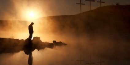 Three Crosses and Silhoutted Person in Prayer at Sunrise