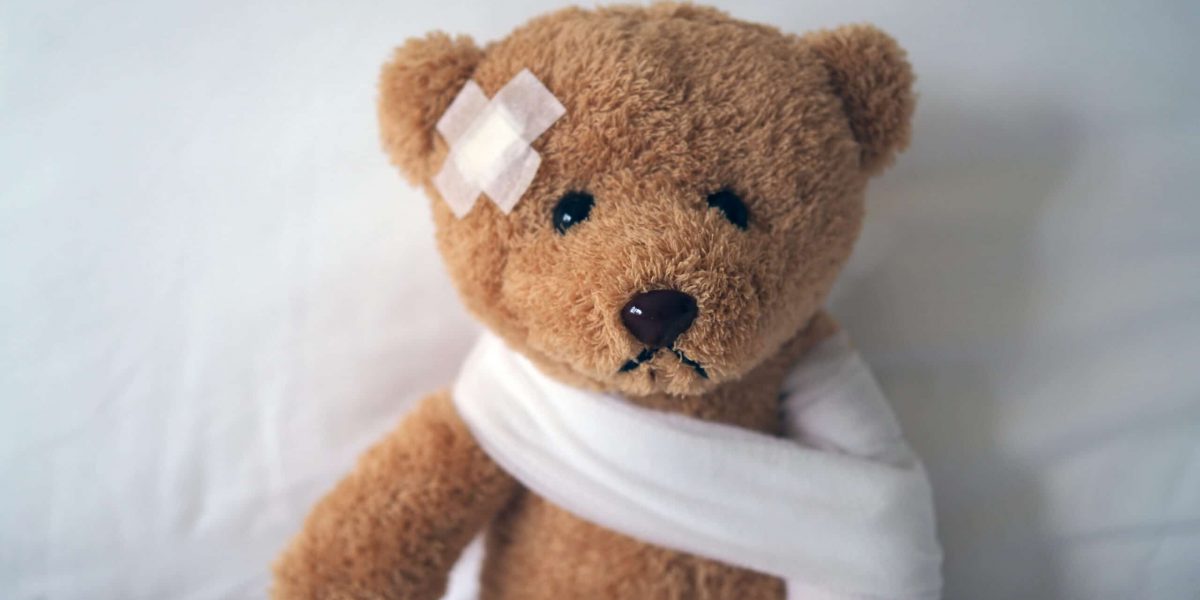 Sad bear doll lying sick in bed with the wound on the head and bandage